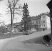 Fotografi mot Hjerströmska gården från hörnet Amiralsvägen och Sjögatan. Man ser en knuttimrad tvåvåningsbyggnad på tomtens norra sida vars brädfodringen håller på att tas ned i samband med rivning.