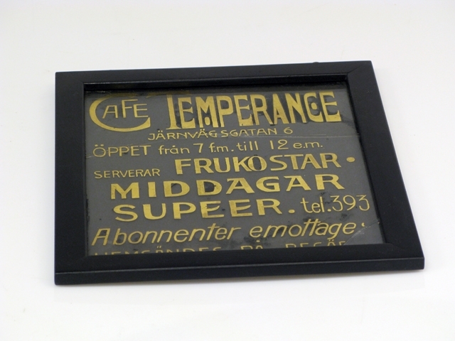 Glasskyltar, 4 st med förgylld text. Bottenfärgen avflagnad på skyltarna.
1) Text: Mjölk ger hälsa, drick därför Säbyholms kontrollerade naturmjölk.
2) Text: Eleganta Automobiler tillhandahålles dygnet om. Tel. 277. A.B. O. Magnusson.
3) Harry Lindberg. Utför alla slags Stenarbeten. Landskrona Kalkbruk, Ständigt lager av kalk.
4) Text: Café Temperance, Frukostar, middagar, supéer.
Inrammad i en svart trätam med krokar upptill för upphängning. Glasskylten har spruckit på två ställen.