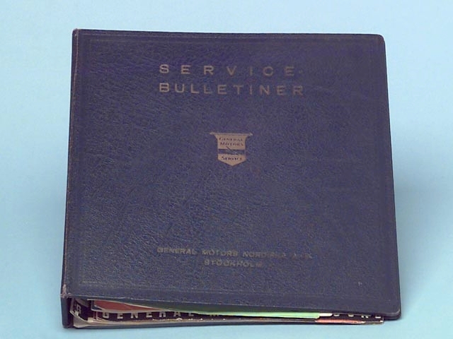 På den blå pärmen står det följande: Service-Bulletiner, General Motors Service, General Motors Nordiska A.B. Stockholm. I pärmen finns det reklambroschyrer på olika fordon, såsom bilar och lastvagnar. På insidan av pärmen står det Ivan Larsson 1946. och konstruktör på General Motors Nordiska A.B i Stockholm 1943.