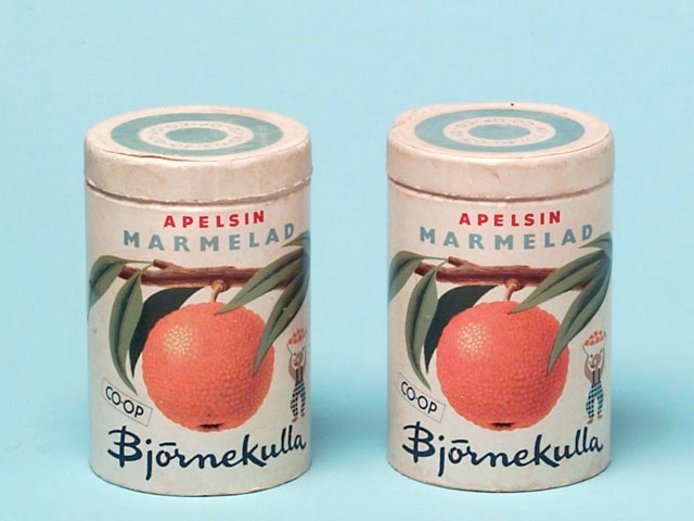 Apelsinmarmeladburk i vaxad papp från Björnekulla. På framsidan står det "Apelsinmarmelad, CO-OP Björnekulla", med bild på en apelsin och en björn som håller en skål med apelsiner. På baksidan finns innehållsdeklaration samt förvaringsanvisningar. Företaget Björnekulla finns i Åstorp och har funnits under det namnet sen 1946.