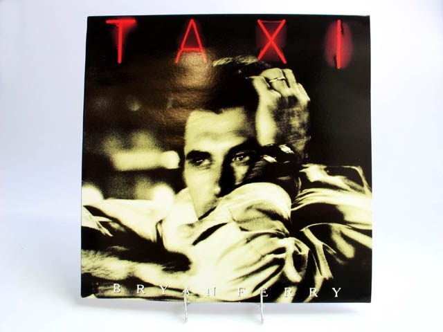 Skivomslag till Bryan Ferrys LP-skiva "Taxi".  Framsidan går i svartvitt med en suddig bild på artisten. Titeln är skriven i röda neon bokstäver, artistens namn i vita tryckbokstäver.
Baksidan går i gult och här finns låtarnas titlar samt en bild i helfigur av artisten. Skivan saknas