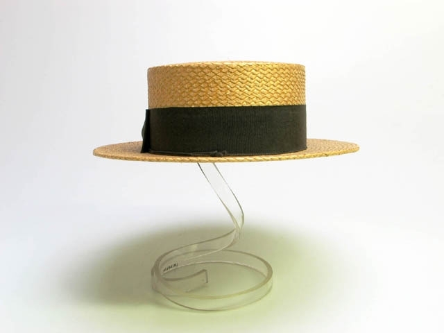 Stråhatt med brunt band och rosett. Insida med läderlinning. Text på läder: AS WORN BY KING GEORGE V. CUSHION FITTING, FRACTIONAL SIZES, POSITIVE VENTILATION, BON TON IVY TRADEMARK, REGISTERED IN ENGLAND AND FOREIGN COUNTRIES, COMFORT HAT. PATENT No 10005-0B. SEE The ELASTIC is tied under Leather To Regulate Size. 1908.
I hatten står sedan: "BATTERSBY & Co LONDON, TRADEMARK, IMPORTED BY EMIL HÖRLITZ, LANDSKRONA.