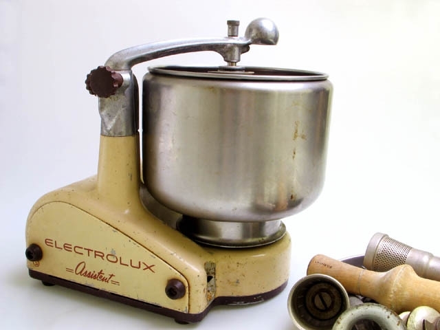 Hushållsassistent av märket Electrolux. Gräddvit med bruna detaljer, metallfärgad arm för montering av verktyg. På sidan står "Electrolux assistent". Metallbricka på baksidan  med texten: MOD. NG1 No S 200408J, ELECTROLUX, V 226, W250. L 32 cm, B 23 cm, H 36 cm.
Tillbehör till hushållassistent.
1) Svart kabel med stickkontakt L 190 cm.
2) Metallskål med hål i mitten. På undersidan finns två metallklämmor fastnitade för att användas till avställning. Diam. 21,7 cm.
3) Tratt i metall. L 16, 8 cm, Diam. 6, 6 cm (i breda änden).
4) Trattformad sil i metall. H 12 cm,  Diam. 6, 3 cm (i breda änden).
5) Del i metall som är till för att riva med. Rör för att fästa i maskin, sedan trattformad med rivjärnshål. H 13, 5 cm, Diam. 5, 5 cm.
6) Trästöt. Olika tjock i olika ändar, men bredast på mitten. För att mata ner livsmedel i beredaren. H 20, 2 cm, Diam. (mitten) 6, 5 cm.
7) Metallkrok (aluminium), vriden som en borr, för att blanda med. L 10 cm.
8) Något att röra med eller möjligen fästa annat verktyg i. Massiv metallklump med breda gängor som en skruv.L 7 cm, Diam. 4, 7 cm.
9) Tratt,  munstycke, i metall. L 3, 8 cm, Diam. 4, 2 cm ( i breda änden).
10) Klämma i metall. Stålpinne som är böjd som ett "U" med en böj nedtill.
11) Köttkvarn. H 19 cm, B 12, 5 cm.
12) Degskrapa i trä och metall.L 18, 5 cm.
13) Blandare i trä. H 19, 5 cm.
14) Skål i metall. H 23 cm, Diam. 24, 5 cm.
Hushållsassistenten skänktes till museet i samband med en utställning på Landskrona  museum som kallades för "HUNDRA!". Denna ägde rum vid millenieskiftet 1900-2000, 1999-12-31 till 2000-03-19. Allmänheten uppmanades då att lämna in det som de ansåg speglade 1900-talet, en sak, en bild, en symbol, ett minne.
Givaren berättar att hushållsassistenten underlättade arbetet i köket.

Köksmaskin Assistent  introducerades 1940 och bifogades då med en speciell samling kristidsrecept. Formgivaren till denna produkt var Alvar Lenning,1897-1980,  som gav maskinen en tidstypisk strömlinjeformad rund design som stod sig ända fram till 1969 med några smärre förändringar.