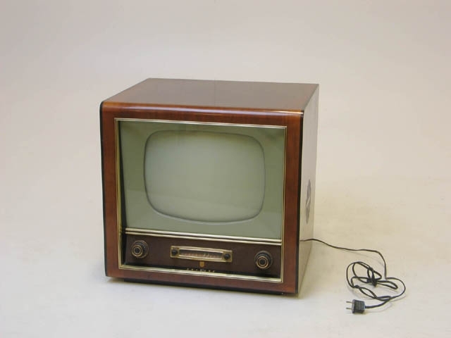 TV från 1956 tillverkad av Philips. Av trä. Varningstext baktill. TV:n tillhörde givarens morfar som bodde i Ekeby. Den var den första TV:n i byn, och grannarna brukade komma och titta, och fick då lägga en krona i kassan för kaffe.
Sverige hade i början bara en sändning per vecka. Danmark hade fler. Man fick in både Italien, Tyskland och Ryssland på TV:n.