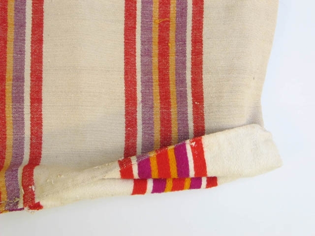 Två stycken kuddvar. Ej stoppade.
1) Grått med rosa, röda, gula och gröna ränder. Mått: L 66,5, B 54,5 cm.
2) Beige med röda, lila och gula ränder. Vänt ut- och inpå. Mått: L 64,5, B 58 cm.
Har tillhört systrarna Andersson, Asmundtorp (Utställningen Systrarna från Asmundtorp). Fyra av de sex systrarna gifte sig inte och deras hemgifter, som bestod av nio kistor med egentillverkade textilier, blev inte använda.