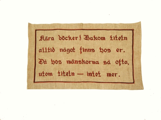 Väggbonad i naturfärgat linne med en bomullsbård i brunt och en röd färg nyans, som är fastsytt 4 cm från kanten.
Bonaden har en broderad text i plattsöm och stjälkstygn i färgerna  röttt och lite brunt.
Följande text är broderat : Kära böcker!  Bakom titeln alltid något finns hos er.
Då hos mänskorna så ofta,  utom titeln - intet mer.