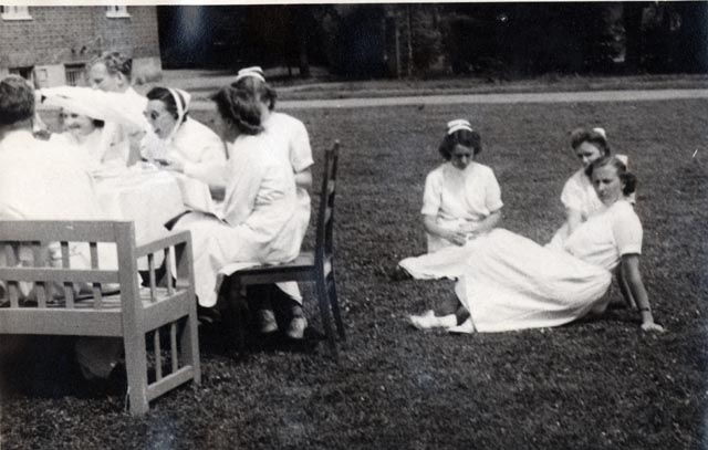 Landskrona sjukhus. Läkare och sjuksystrer sitter i trädgården och fikar.