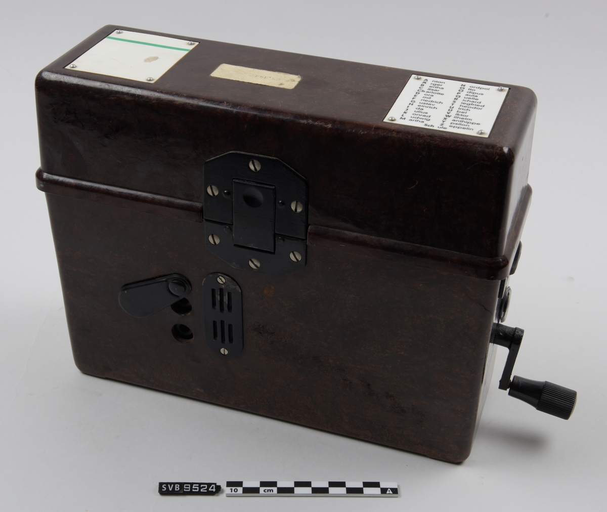 Felttelefon i brun boks. Boksen har et lokk som er henglset langs baksiden. På fremsiden er det en en lås av metall. På toppen av lokket er det to hvite plansjer, den ene har fonetisk alfabet. På innsiden av lokket er det to hvite plansjer med diagrammer. På hver side av boksen er det metallbraketter. Nederst på høyre side av boksen er det en sveiv. På fremsiden er det to hull dekket med et plastdeksel som er festet til boksen i ene enden. Dette kan roteres bort fra hullene.
Inne i boksen ligger det et telefonrør.på en base av sort metall. Telefonrøret har en ledning som er festet til basen med en kontakt. Under basens venstre side står det et batteri. På midten av basen er det to metallbolter.