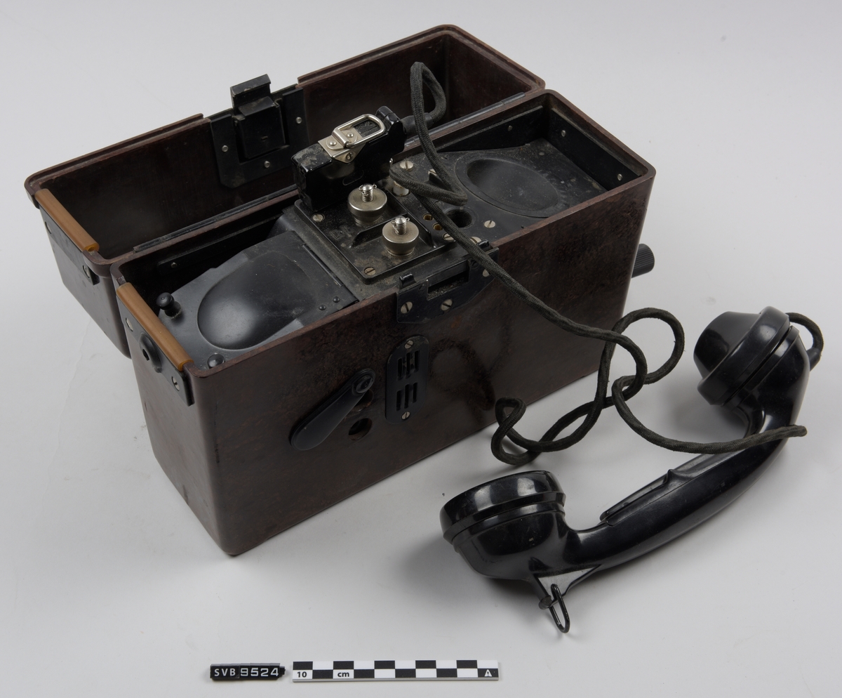 Felttelefon i brun boks. Boksen har et lokk som er henglset langs baksiden. På fremsiden er det en en lås av metall. På toppen av lokket er det to hvite plansjer, den ene har fonetisk alfabet. På innsiden av lokket er det to hvite plansjer med diagrammer. På hver side av boksen er det metallbraketter. Nederst på høyre side av boksen er det en sveiv. På fremsiden er det to hull dekket med et plastdeksel som er festet til boksen i ene enden. Dette kan roteres bort fra hullene.
Inne i boksen ligger det et telefonrør.på en base av sort metall. Telefonrøret har en ledning som er festet til basen med en kontakt. Under basens venstre side står det et batteri. På midten av basen er det to metallbolter.