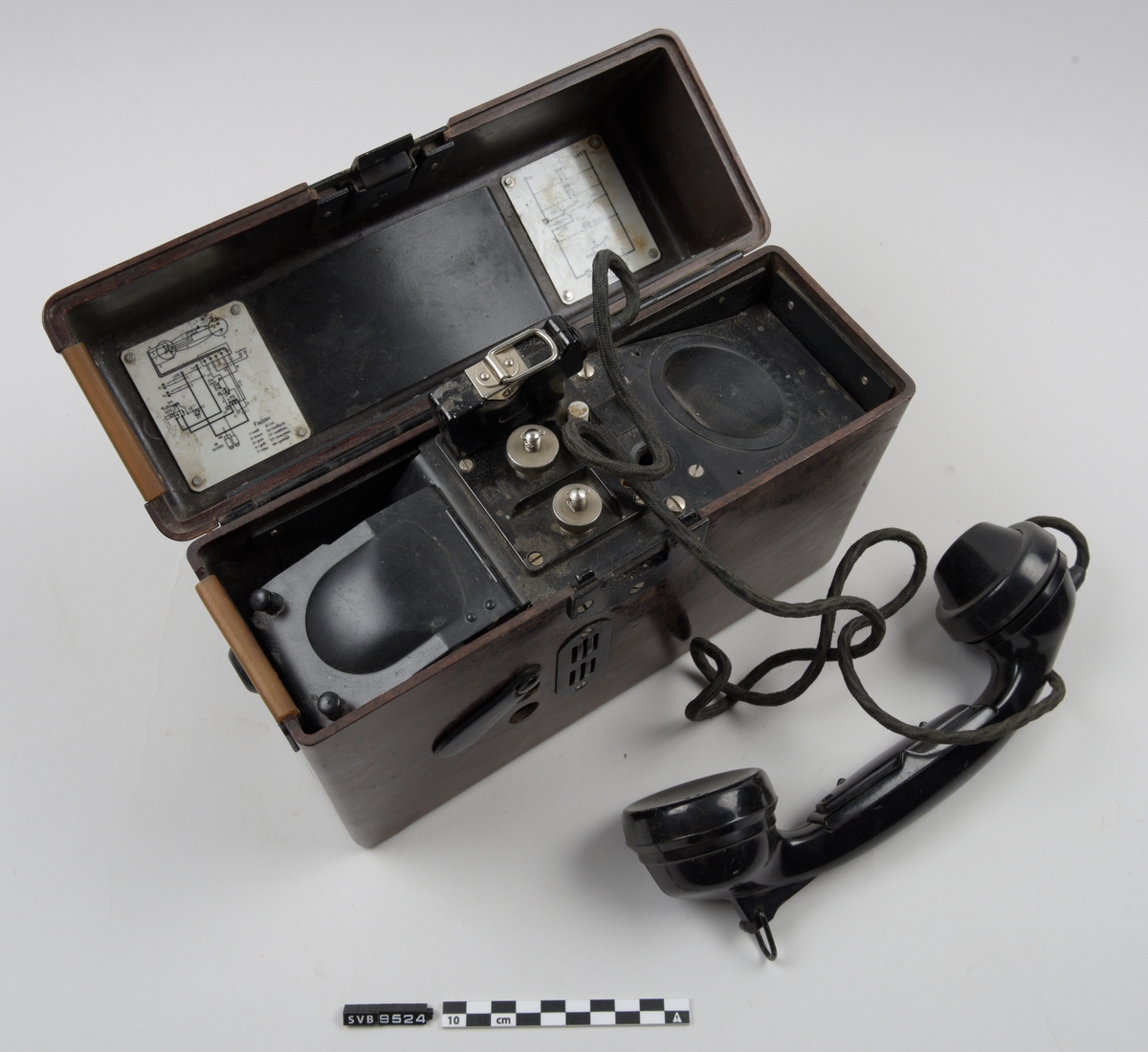 Felttelefon i brun boks. Boksen har et lokk som er henglset langs baksiden. På fremsiden er det en en lås av metall. På toppen av lokket er det to hvite plansjer, den ene har fonetisk alfabet. På innsiden av lokket er det to hvite plansjer med diagrammer. På hver side av boksen er det metallbraketter. Nederst på høyre side av boksen er det en sveiv. På fremsiden er det to hull dekket med et plastdeksel som er festet til boksen i ene enden. Dette kan roteres bort fra hullene.
Inne i boksen ligger det et telefonrør.på en base av sort metall. Telefonrøret har en ledning som er festet til basen med en kontakt. Under basens venstre side står det et batteri. På midten av basen er det to metallbolter.