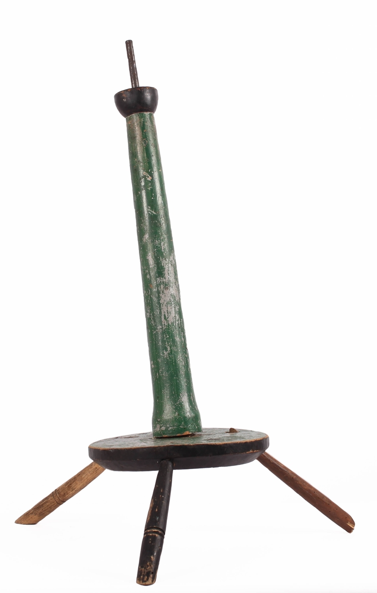 Liten trekrakk / stativ, til å feste på storkarden (grøypkarden) for karding av ull.  Krakken har tre føtter, og hull i midten. Den er svartmalt på undersiden og grønnmalt ellers, i samme farge som karden (neb.g01410).