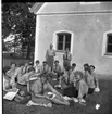 Kvinnliga scoutledare sitter med anteckningsblock i en ring på en gräsmatta utanför gamla tingshuset på Visingsö, de vänder sig mot fotografen. Bakom dem står två manliga scoutledare.