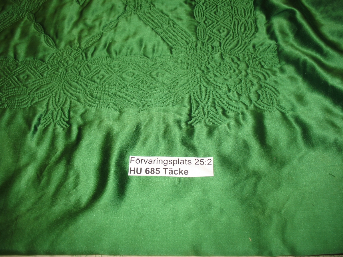 Täcke, 245 x 226, grönt blankt siden från Liberty.
I kanten rik bård i sticksöm. Över spegeln rikt ytmönster med stora stjärnor, allt sticksöm i grönt silke. Foder vitt fint bomullstyg.