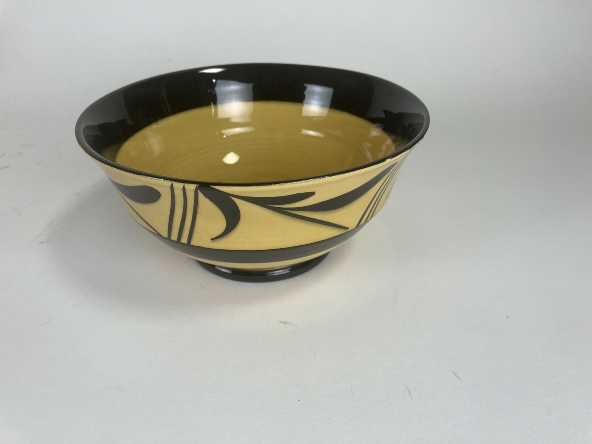 Bolle til mokkaservise, gult med svart pynt, bestående av 30 deler. Serviset er brukt som dokkestell. Dokkestell ble gitt til jenter til lek som forberedelse til voksenlivet. 