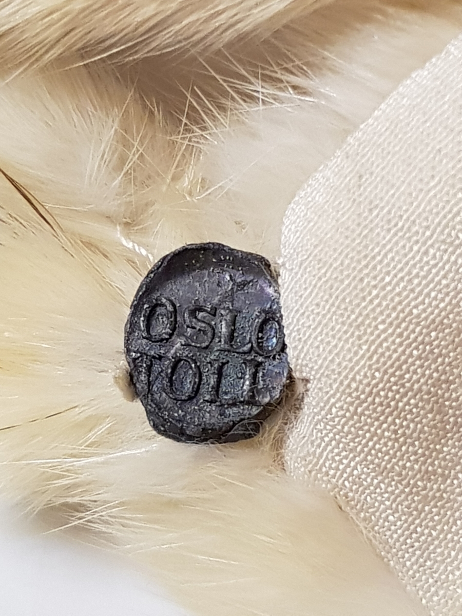 Midjelang cape, med rund, tettsluttende halsringning og lukning med to hekter midt foran. Pelsstykkene er sammensydd slik at det dannes vertikale, smale felt, og de rette skuldrene er formet ved skuldersømmer. Capen er kantet med tette frynser av røyskatthaler i nederkant og helföret med benhvit silke. På innsiden, nede i front, en tollplombering.