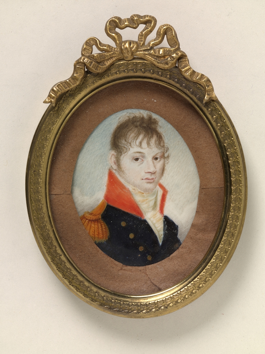 Portrett av ung mann i uniform. Lyst brunt hår, krøllet ned i pannen. Kinnskjegg. Brune øyne, lys hudfarge. Blå jakke med gullknapper og epålett. Rød, høy stiv krave, hvitt halsbind.