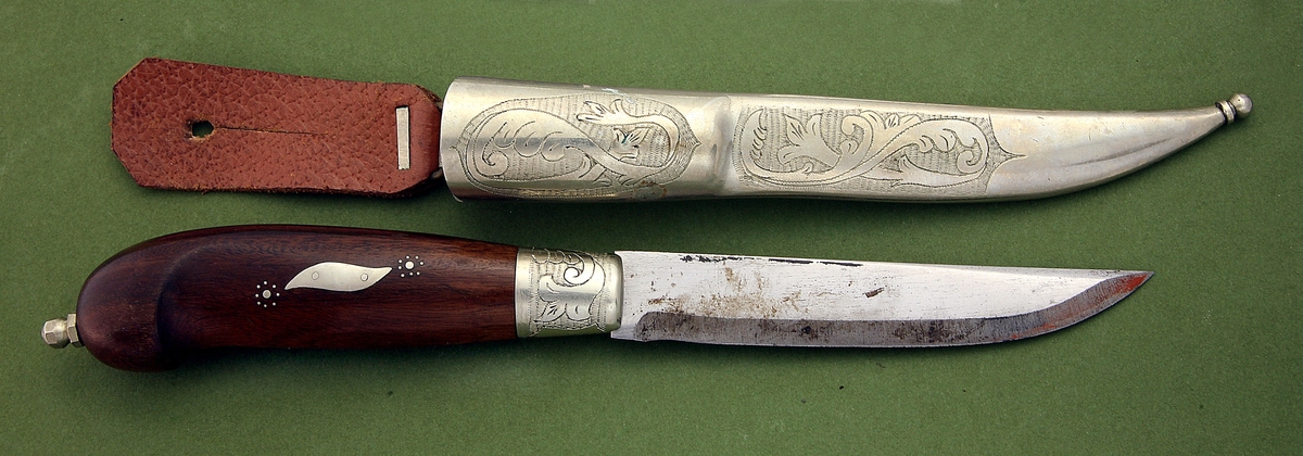 Kniv med slire. Kniv med treskaft, mangefasettert endekule, og skaftholk i nysølv. Stiftdekor og marketeri - nysølvplate. Trambulering på skaftholk. Slire i nysølv, to felt med akantustrambulering, og liten endekule. Lærhempe med utydelig blyantskrift.
Form: Typisk Hedenbergkniv
