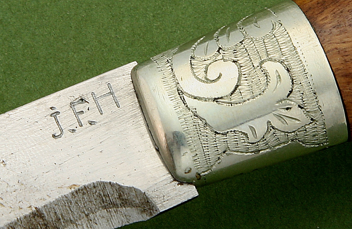 Kniv med slire. Kniv med treskaft, mangefasettert endekule, og skaftholk i nysølv. Stiftdekor og marketeri - nysølvplate. Trambulering på skaftholk. Slire i nysølv, to felt med akantustrambulering, og liten endekule. Lærhempe med utydelig blyantskrift.
Form: Typisk Hedenbergkniv
