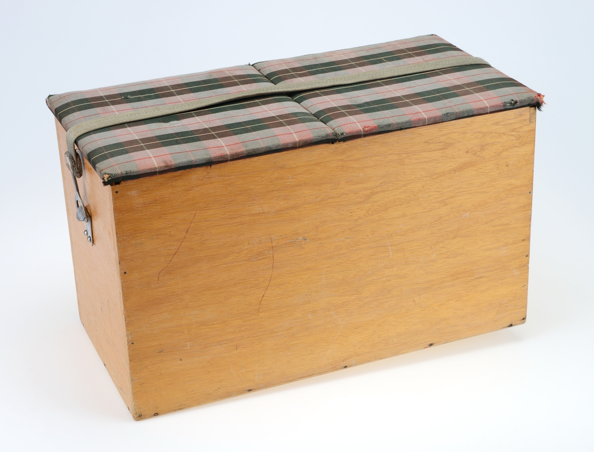 Kombinert kurv og benk med kopper og kar. Kurven inneholder en kakeboks, fire plastkopper, to glass, åtte fat, fire bokser og en eske med bestikk. Klaffene er trekt i stoff og fungerer som benk når den er lukket.