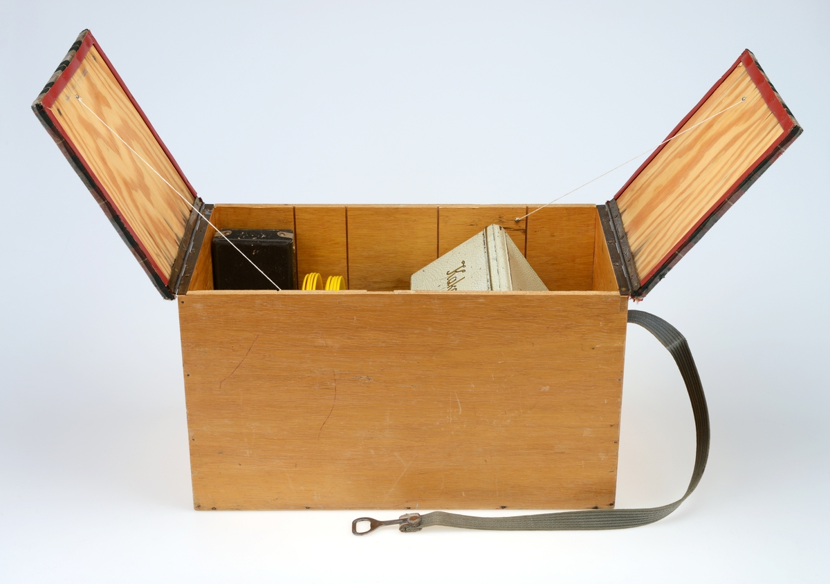 Kombinert kurv og benk med kopper og kar. Kurven inneholder en kakeboks, fire plastkopper, to glass, åtte fat, fire bokser og en eske med bestikk. Klaffene er trekt i stoff og fungerer som benk når den er lukket.