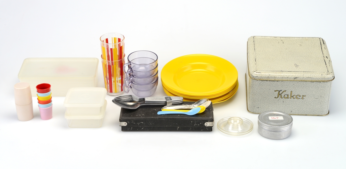 Kombinert kurv og benk med kopper og kar. Kurven inneholder en kakeboks, fire plastkopper, to glass, åtte fat, fire bokser og en eske med bestikk. Klaffene er trekt i stoff og fungerer som benk når den er lukket.