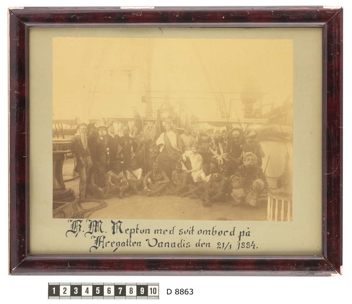 Bilden föreställer en grupp fantasifull utklädda sjömän som har samlats på däck inför neptunifesten vid passerandet av linjen 21/1 1884 ombord på fregatten Vanadis världsomsegling 1883-85.