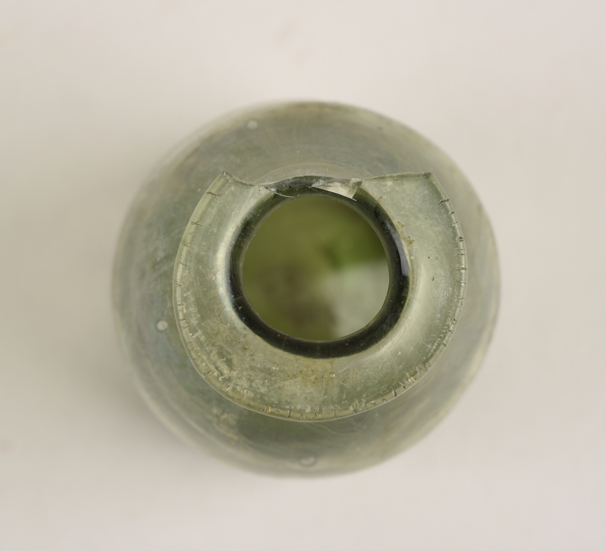 Sylindriskformet glassflaske. Deler av randen mangler. På toppen av flasken er det et sirkelformet hull. Hullet har en diameter på 1,2 cm. Flasken er lys grønn i farge.