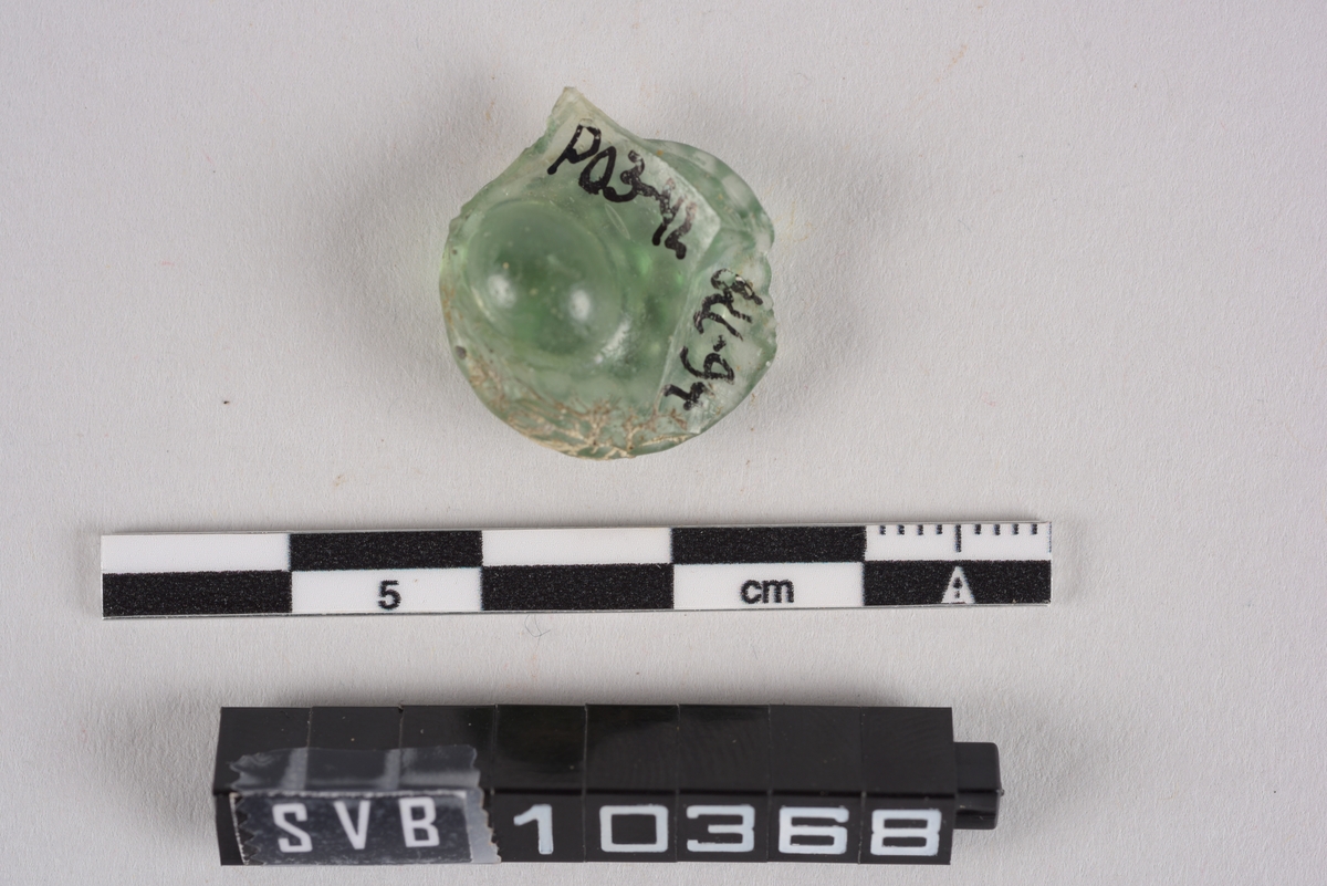 Fragment av glass. Grønn farge. Det er dekor på den ene siden. Dekoren er som små konvekse halvkuler.