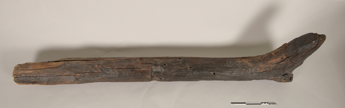 Stevn av båt av treverk, med fem hull for jernbolter. To jernbolter bevart.  Merket med tusj som "III-23".