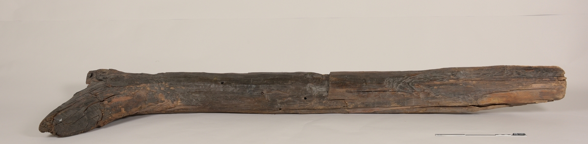 Stevn av båt av treverk, med fem hull for jernbolter. To jernbolter bevart.  Merket med tusj som "III-23".
