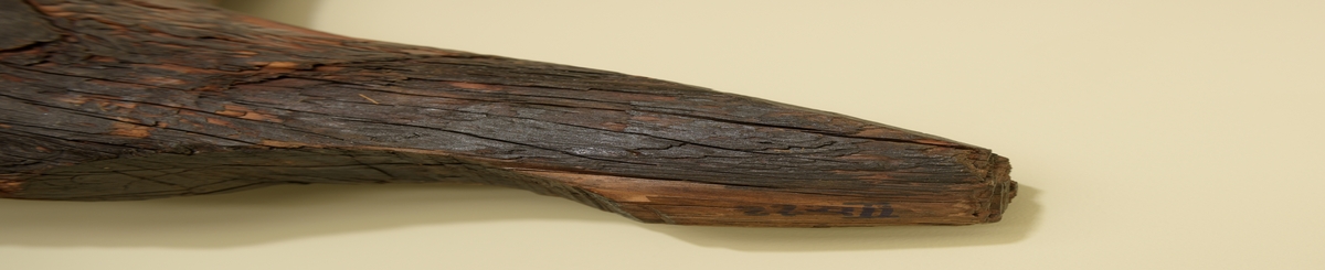Stevn av båt av treverk, med fem hull for jernbolter. To jernbolter bevart.  Merket med tusj som "III-23".