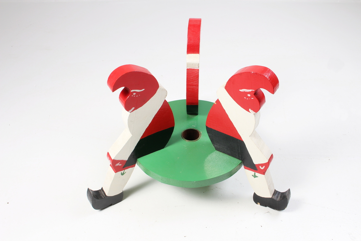 Juletrefot med tre nisser som sitter på en rund plate. Utskåret av tre.