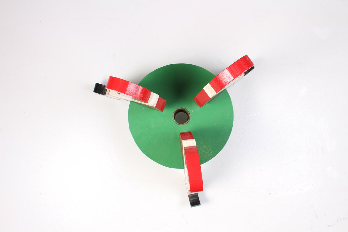 Juletrefot med tre nisser som sitter på en rund plate. Utskåret av tre.