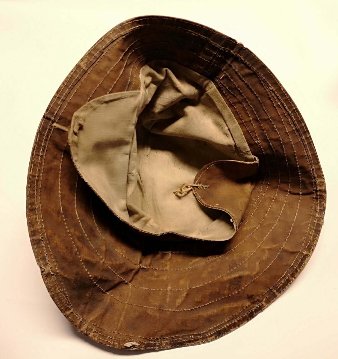 Brun sydvest av oljet lerret. Pullen består av seks kiler sydd sammen i en topp. Bremmen er i et stykke. Bremmen er avstivet, sannsynligvis ved at det er sydd flere lag med lerret over hverandre. Maskinsøm. Inne i pullen er det fôr av bomullsstoff. Øreklaffene er sydd sammen med pullen på innsiden. Rester av hyssing på øreklaffene. 