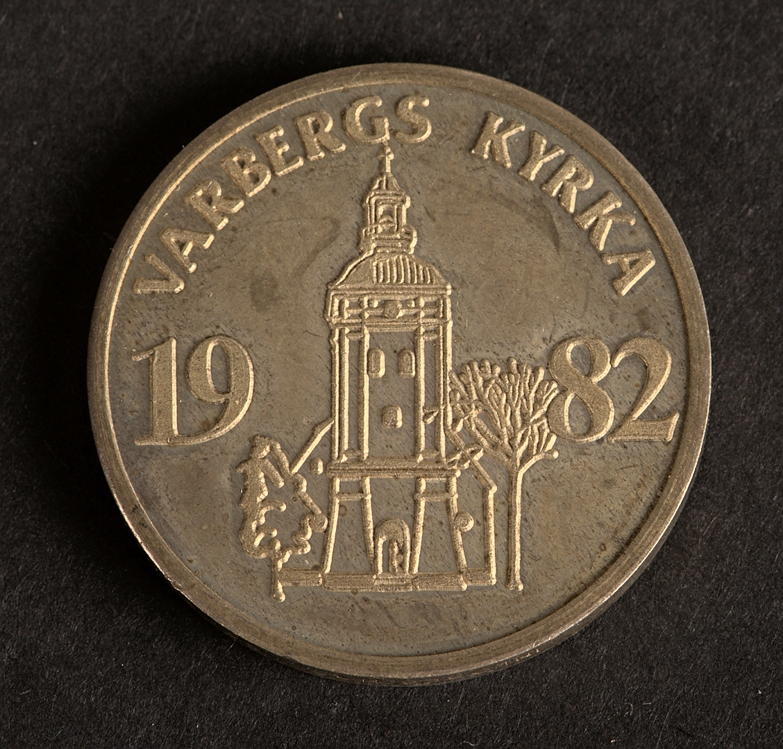 Åtsida: Varbergs vapen med omgivande text: "LOKALMYNT FÖR VARBERGS KOMMUN 150 KR". Frånsida: Varbergs kyrka med omgivande text: "VARBERGS KYRKA 1982". Kontrollstämpel m.fl. stämplar på kanten.
