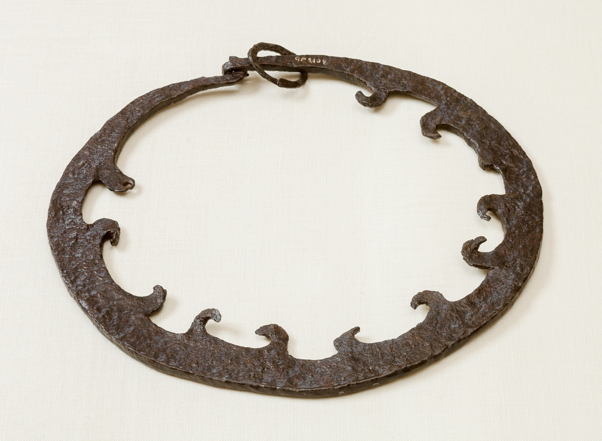 Ring av järn med på insidan kloformiga böjda flikar. Plattjärn, hakad samman vid ena sidan med ändarna krökta, innerkaten har 12 stycken hullinglika hakar, en av dem är avbruten och en är trubbig och med ett litet hål genomborrat.

Härtill har hört en nu förlorad torshammare.