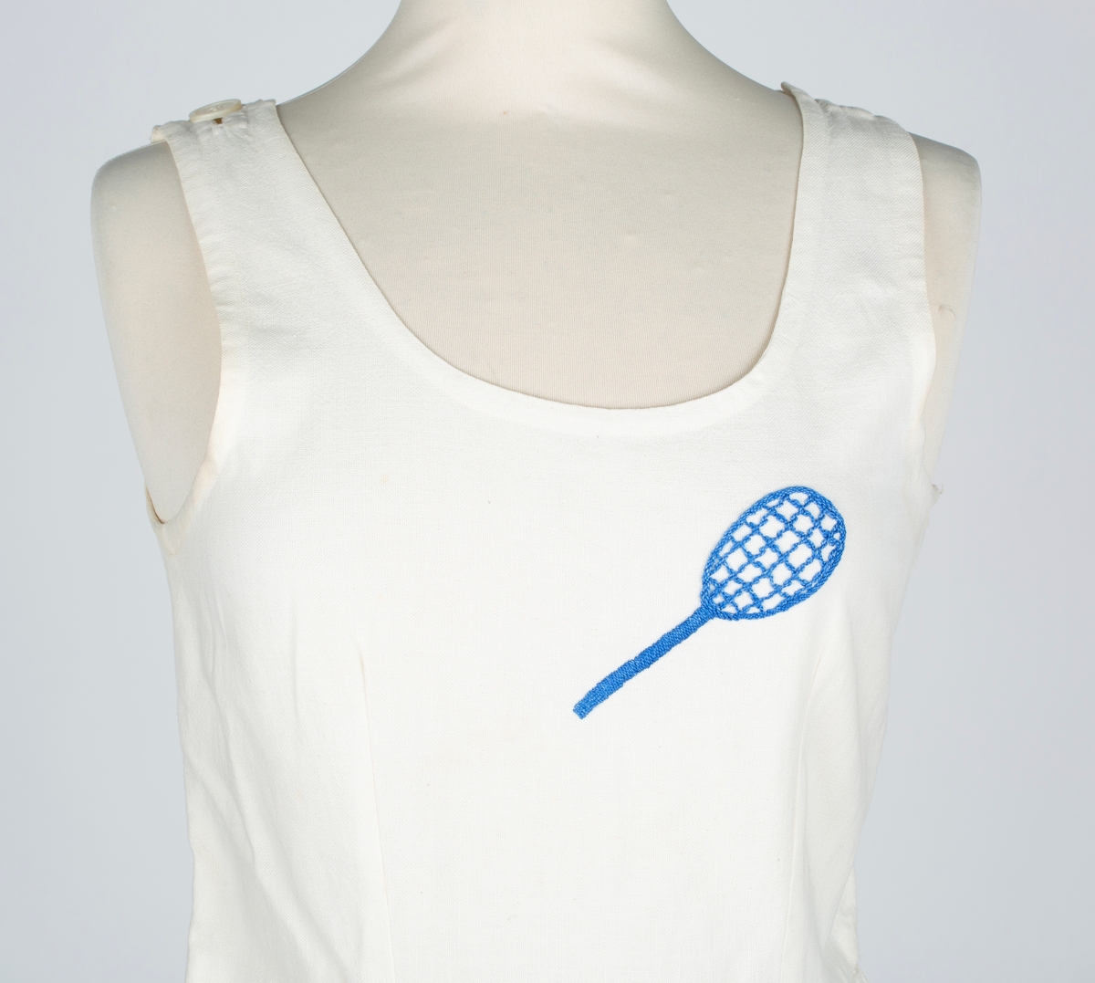 Hjemmesydd. Vid, buet halsringing, uten ermer, lengdesnitt foran og bak, avdelt i livet , bukseskjørt. Brodert tennisrekkert på venstre bryst. 

Brukt av søstrene Hilda og Olga Ambjørnrud.

Olga Ambjørnrud: "Brukt på Drøbak Tennisbane. Tennisbanen lå på tomta til Sentrumsbygget (nær torget).
Tennisbanen var veldig opptatt; måtte bestille tiime. Der var store turneringer i begynnelsen av 1930 årene. Hilda var veldig ivrig. Vanligvis spilte Hilda og jeg sammen. Vi spilte ikke i klubb, vi spilte når vi kunne få plass.
Tenniskjolen var av de første som kom på markedet"