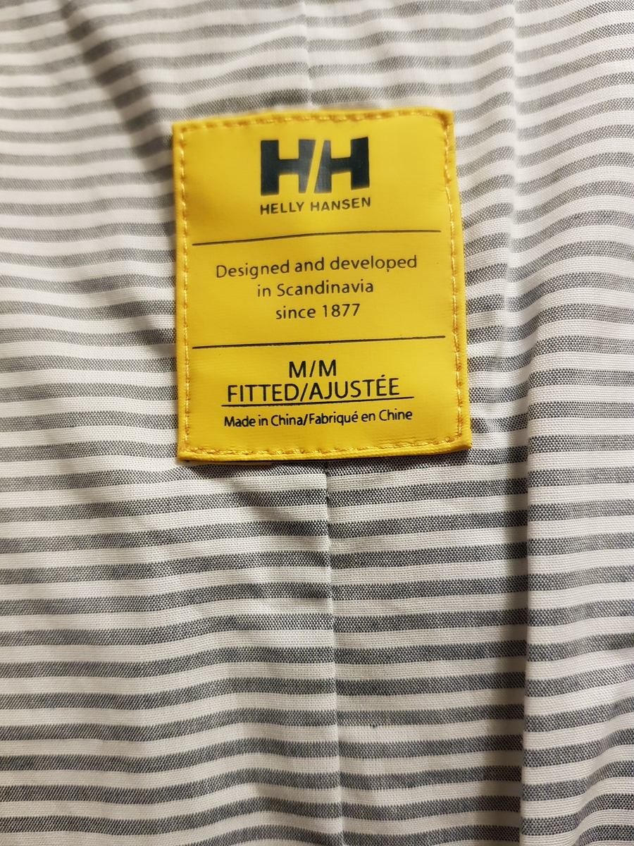 Gul, halvlang, myk regnjakke med hette, preget med HH på alle knappene midt foran. Midt bak et bærestykke, som er sveiset fast på to plasser. Også sveiset midt bak, og utstyrt med en motfold rett nedenfor livet. Løst, sveiset belte og sydde hemper. Skuldersømmen er flyttet litt foran. Gummiert, gult HH merke er innsydd. Lommer med klaff. Trykkknapp midt på klaffen, nagler på begge sider av klaffen. Snor i hetten, med stoppere. Lukkes midt foran med gule trykknapper preget med HH. Trykknapp-regulering nederst på erme. Jakken er fôret med smalstripet hvit og lys grått stoff. Ermene er fôret med svart fôr, Nederst på ermet er det sydd på 5,5 cm fôr lik jakken. Jakkens sømmer er sveiset.