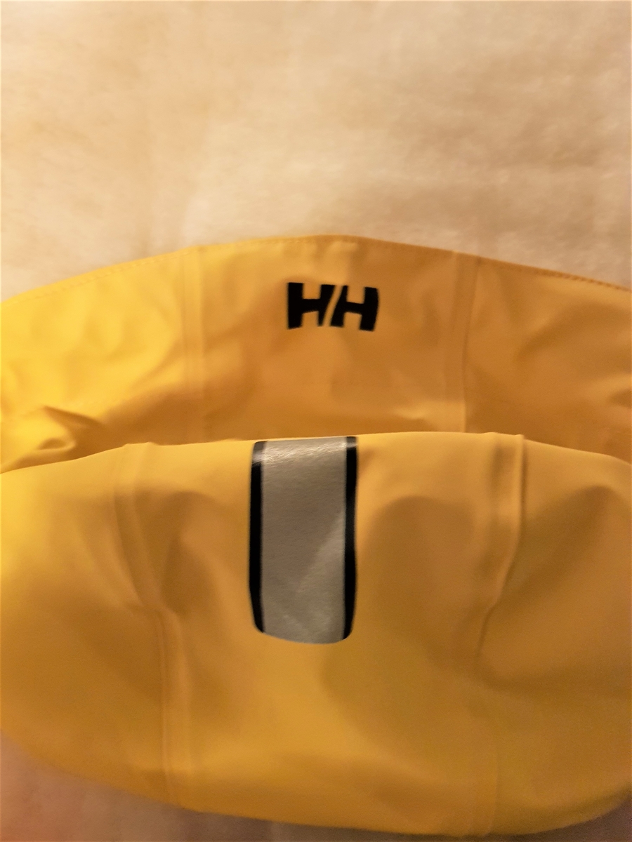 Gul, halvlang, myk regnjakke med hette, preget med HH på alle knappene midt foran. Midt bak et bærestykke, som er sveiset fast på to plasser. Også sveiset midt bak, og utstyrt med en motfold rett nedenfor livet. Løst, sveiset belte og sydde hemper. Skuldersømmen er flyttet litt foran. Gummiert, gult HH merke er innsydd. Lommer med klaff. Trykkknapp midt på klaffen, nagler på begge sider av klaffen. Snor i hetten, med stoppere. Lukkes midt foran med gule trykknapper preget med HH. Trykknapp-regulering nederst på erme. Jakken er fôret med smalstripet hvit og lys grått stoff. Ermene er fôret med svart fôr, Nederst på ermet er det sydd på 5,5 cm fôr lik jakken. Jakkens sømmer er sveiset.
