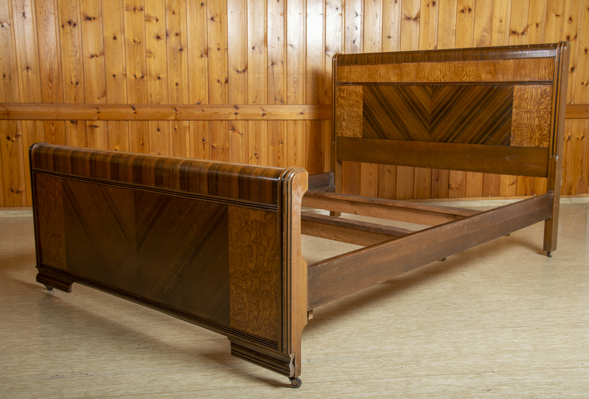 Seng i Art Deco stil. Består av hodegavl, endegavl, to sidestykker og tre tverrstykker til sengebunn. Hodegavlen er høyere enn endegavlen. Gavlstykkene er dekorert med felt i ulike typer finér, antatt bjørk og mahogni. Gavlene har avrundet kant på toppen i mørk finér, et felt med mørk finér i senter med finéren lagt i fiskebensmønster, som er rammet inn av et felt med lysere finér på hver side. Benene har påmontert små hjul. Skadet finér på hodegavl.