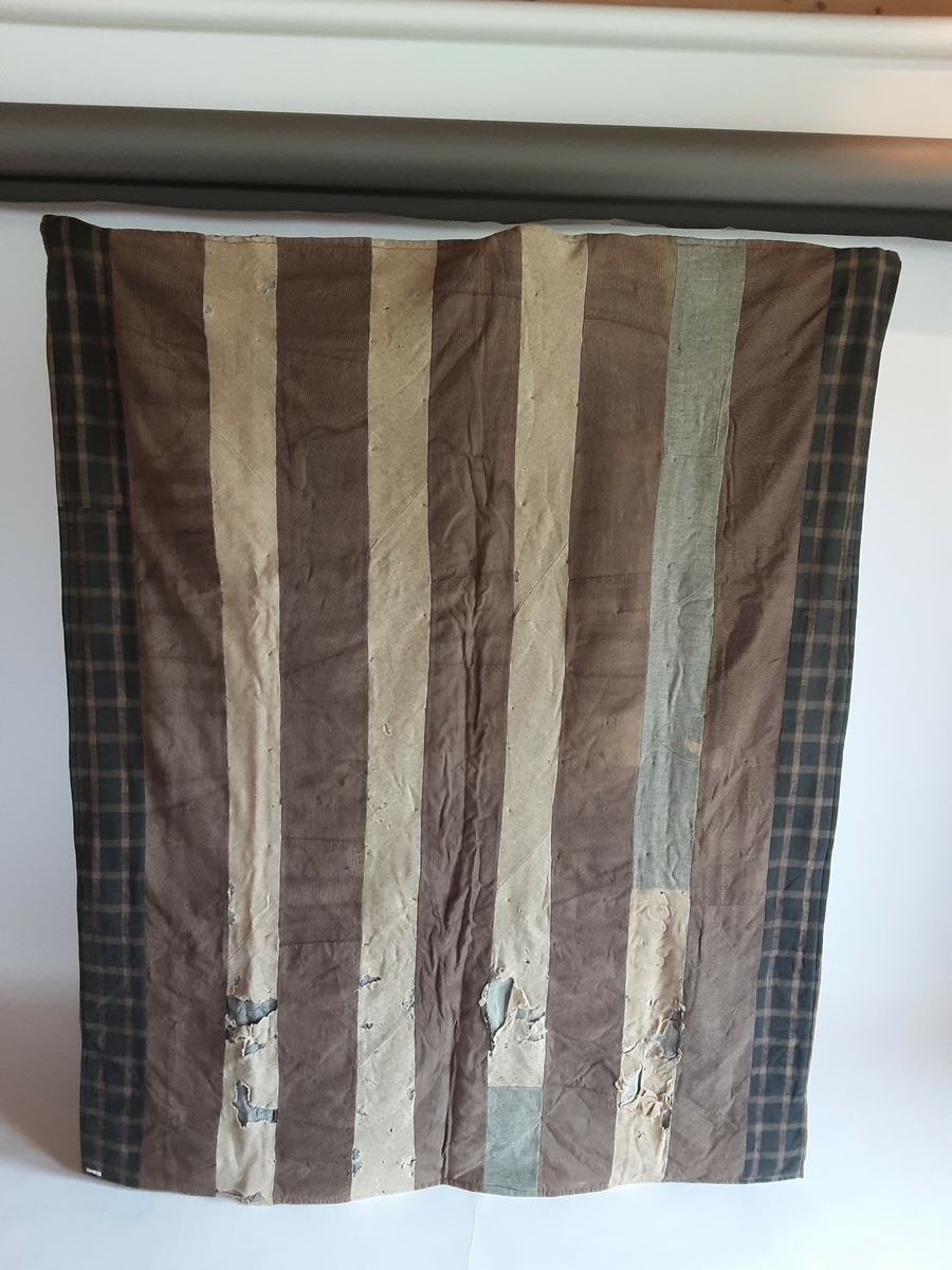 Vatt-teppe. Quiltet, brune nyanser. Satt sammen av trekanter. Ulike litt grove stofftyper (ull?). Pyntet med knyter laget av rødt og beige garn. De samme stoffene er satt sammen til striper og danner baksiden på teppet. Huller i stoffet enkelte steder.