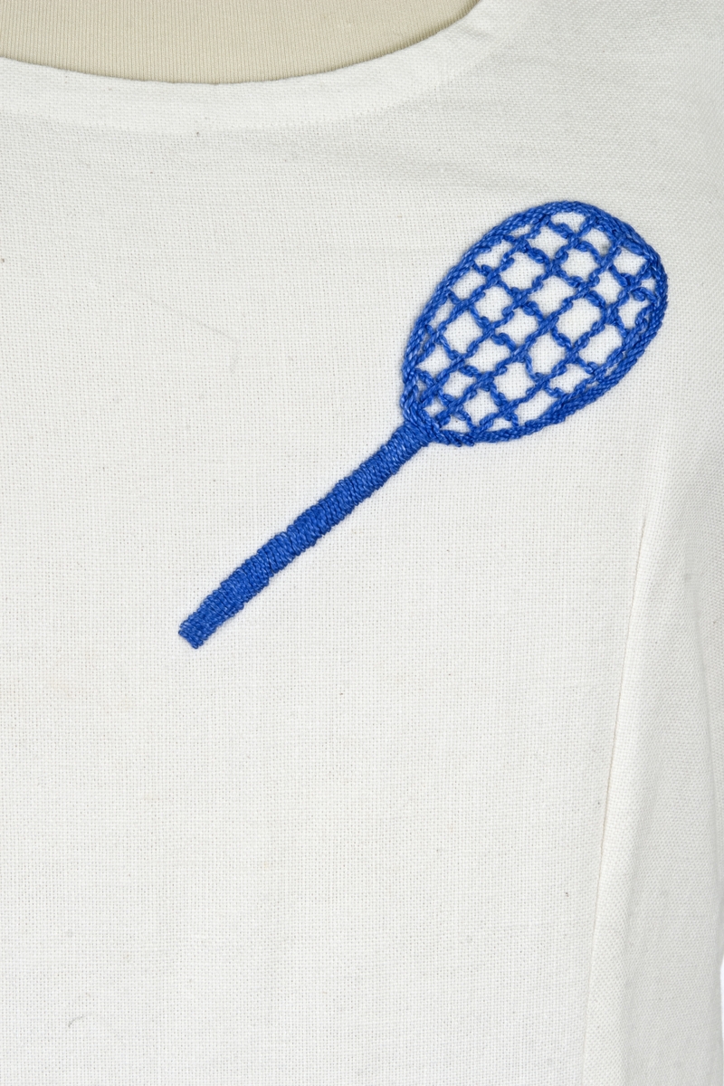 Hjemmesydd. Vid, buet halsringing, uten ermer, lengdesnitt foran og bak, avdelt i livet , bukseskjørt. Brodert tennisrekkert på venstre bryst. 

Brukt av søstrene Hilda og Olga Ambjørnrud.

Olga Ambjørnrud: "Brukt på Drøbak Tennisbane. Tennisbanen lå på tomta til Sentrumsbygget (nær torget).
Tennisbanen var veldig opptatt; måtte bestille tiime. Der var store turneringer i begynnelsen av 1930 årene. Hilda var veldig ivrig. Vanligvis spilte Hilda og jeg sammen. Vi spilte ikke i klubb, vi spilte når vi kunne få plass.
Tenniskjolen var av de første som kom på markedet"