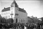 På Järnvägstorget i Jönköping syns människor och lastade vagnar, kanske är bilden tagen vid någon av de marknader som förr hölls här. Till höger om Post- och Telegrafhuset ligger Järnvägshotellet och Krönleins bryggeri.