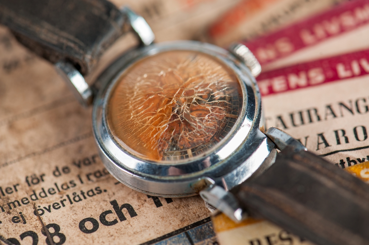 Armbandsur med brunt läderarmband. Rostangripen urtavla bakom bukigt krackelerat glas.