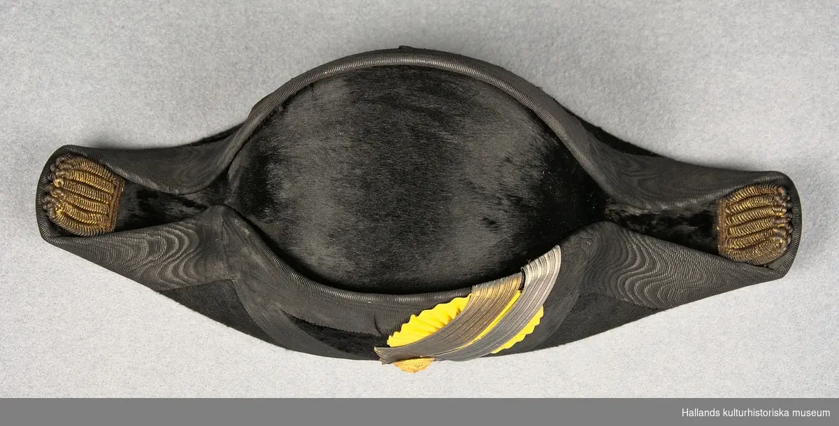 A: Hattask av papp målad i en lilablå nyans. På ovansidan ett emblem från tillverkaren och på baksidan ett snöre.

B: Befällshatt av bicornetyp. Hatten är klädd med svart fälb och ett svart mönstrat sidenband. På höger sida sitter en gul sidenkokard under dubbla band - ett i guld och ett i silver. På höger sida även en guldknapp med flottans vapen bestående av ett ankare och tre kronor. Guldfärgade tassar bak- och framtill på hatten. Hakrem av svart läder.