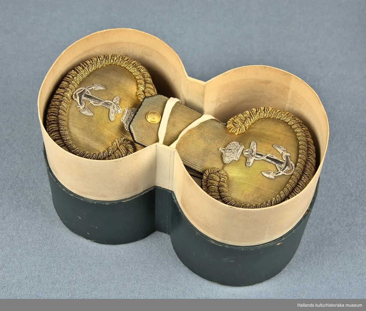 A:1-2: Epåletter för personal av officerrang inom flottan. Undersidan på epåletterna är klädda med en matta av mörkblå samet och översidan med ett band av guldgalon. På epåletthalsen sitter en liten knapp med flottans vapen och på klaffen finns flottans vapen broderad i silvertråd. Epåletterna är även försedda med fransar i tunn guldsnodd.

På undersidan finns en hake (för infästning på vapenrock) av guldmetall med stämpeln: "F&Co".

B: Förvaringsask av papp målad i en mörkgrön nyans.