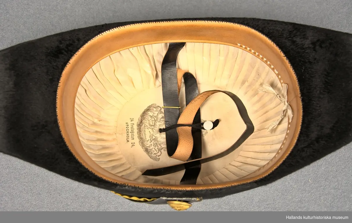 A: Hattask av papp målad i en lilablå nyans. På ovansidan ett emblem från tillverkaren och på baksidan ett snöre.

B: Befällshatt av bicornetyp. Hatten är klädd med svart fälb och ett svart mönstrat sidenband. På höger sida sitter en gul sidenkokard under dubbla band - ett i guld och ett i silver. På höger sida även en guldknapp med flottans vapen bestående av ett ankare och tre kronor. Guldfärgade tassar bak- och framtill på hatten. Hakrem av svart läder.