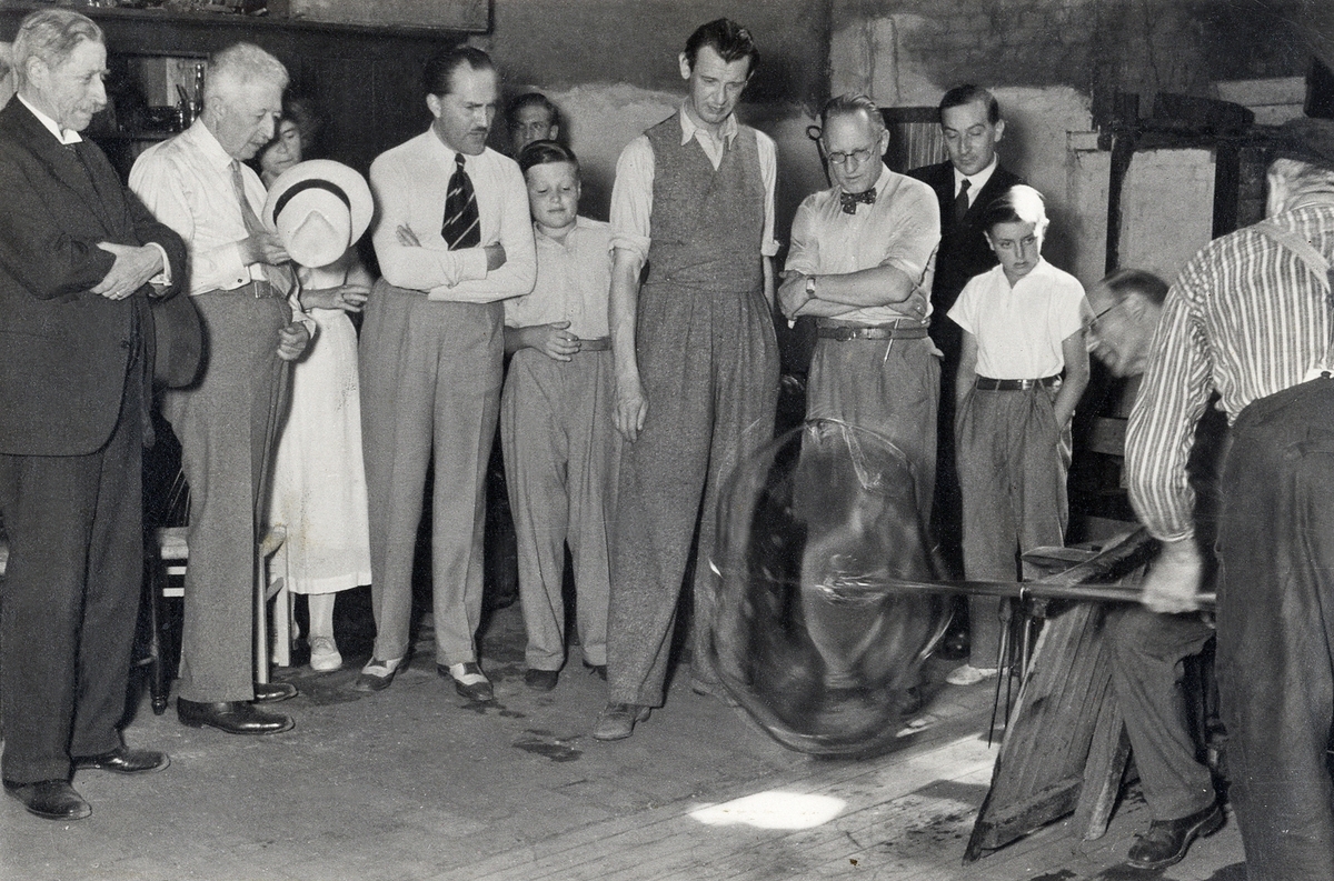 Orrefors glasbruk.
Hyttmästare Gustaf Bergqvist med publik i hyttan. Fr. v.: Verner von Heidenstam, prins Eugen, okänd, Henning Beyer, okänd, okänd, Vicke Lindstrand, Edward Hald, okänd, okänd, Gustaf Bergqvist.