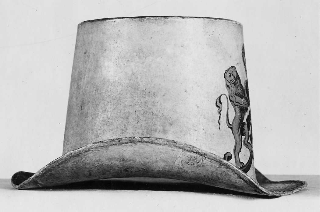 Hatt tillverkad av papp som målats med en crémegul färg. Framtill försedd med svensk-norska riksvapnet i färg. Foder av bomullstyg, 115 mm brett och dragsko.