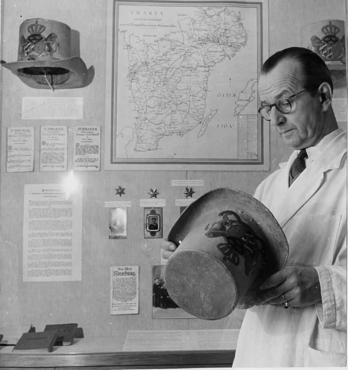 Hatt tillverkad av papp som målats med en crémegul färg. Framtill försedd med svensk-norska riksvapnet i färg. Foder av bomullstyg, 115 mm brett och dragsko.